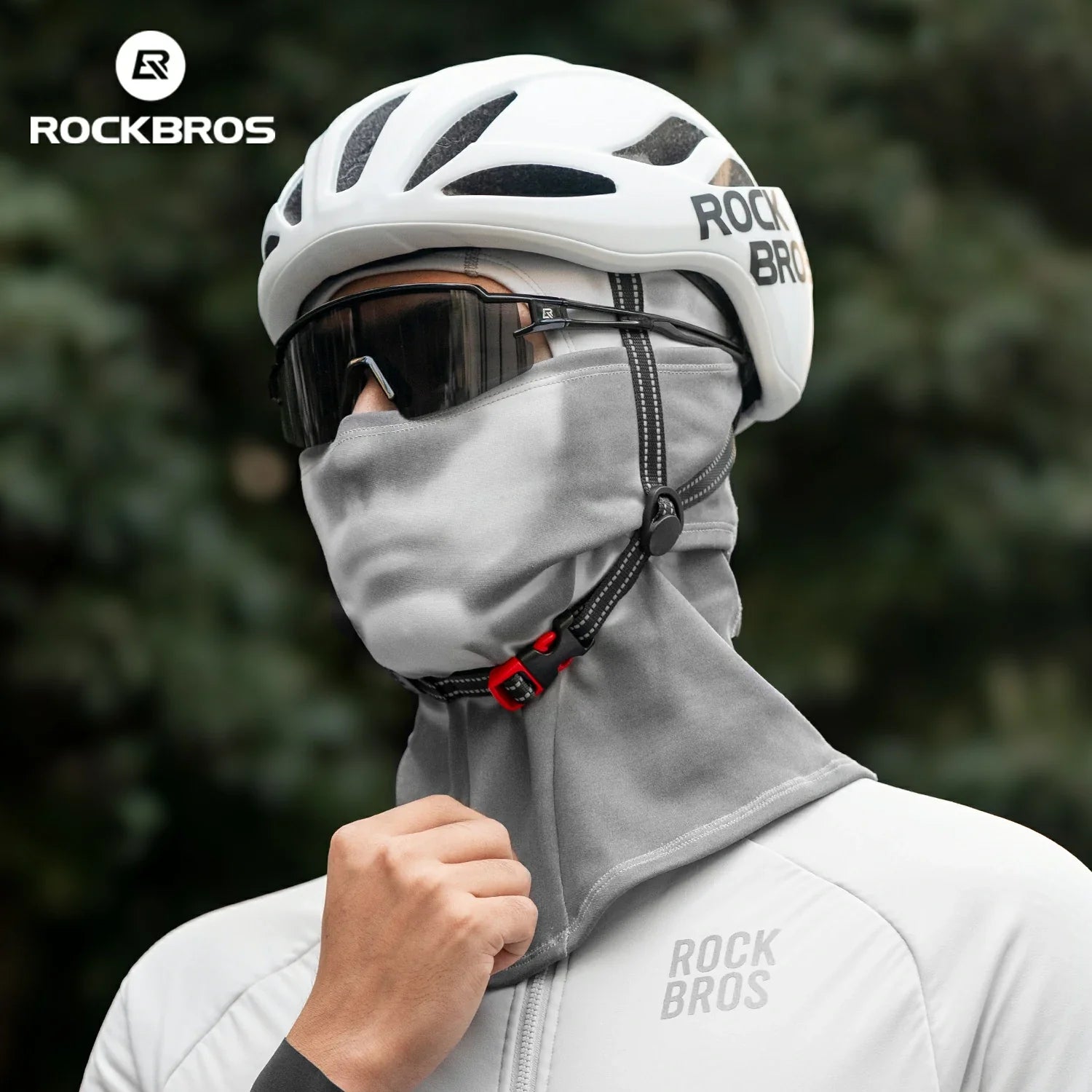 Person wearing a white helmet, gray balaclava, and white jacket with 'RockBros' branding against a blurred green background.#color_Dark Gray