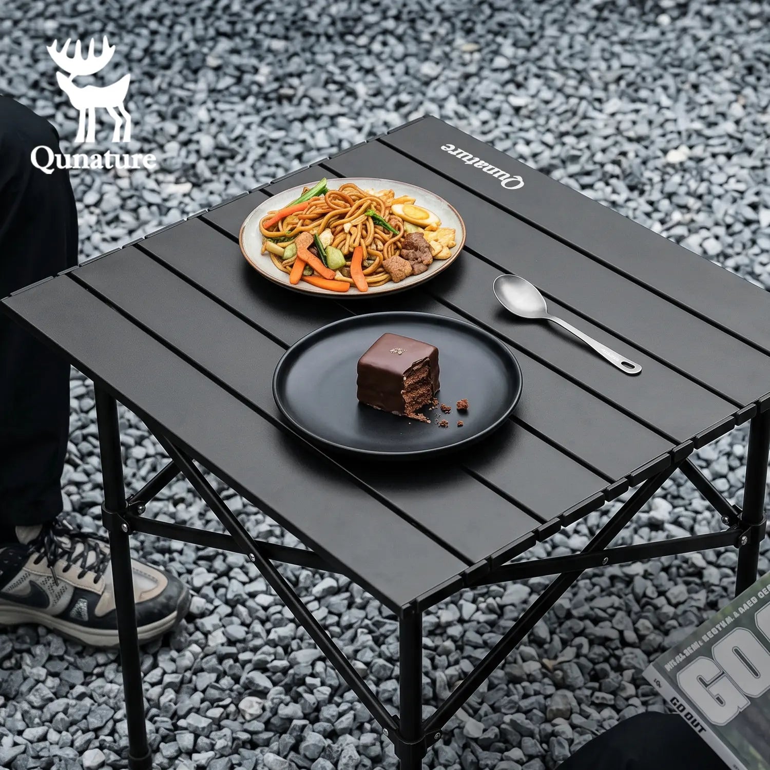 Black folding table with food on a gravel surface, featuring the Qunature brand.