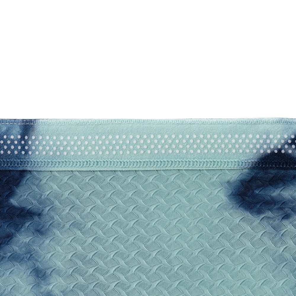 A close-up of a textured fabric with a diamond-weave pattern in light blue and dark blue tie-dye, featuring a dotted elastic band at the top.