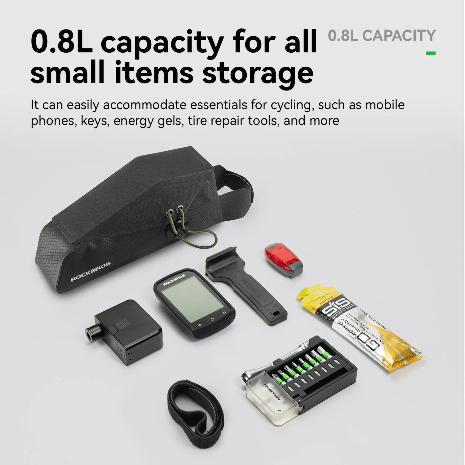 A black bikepacking bag shown with several cycling essentials arranged on a light gray background, including a GPS device, battery, energy gel, small tool, and a strap. 