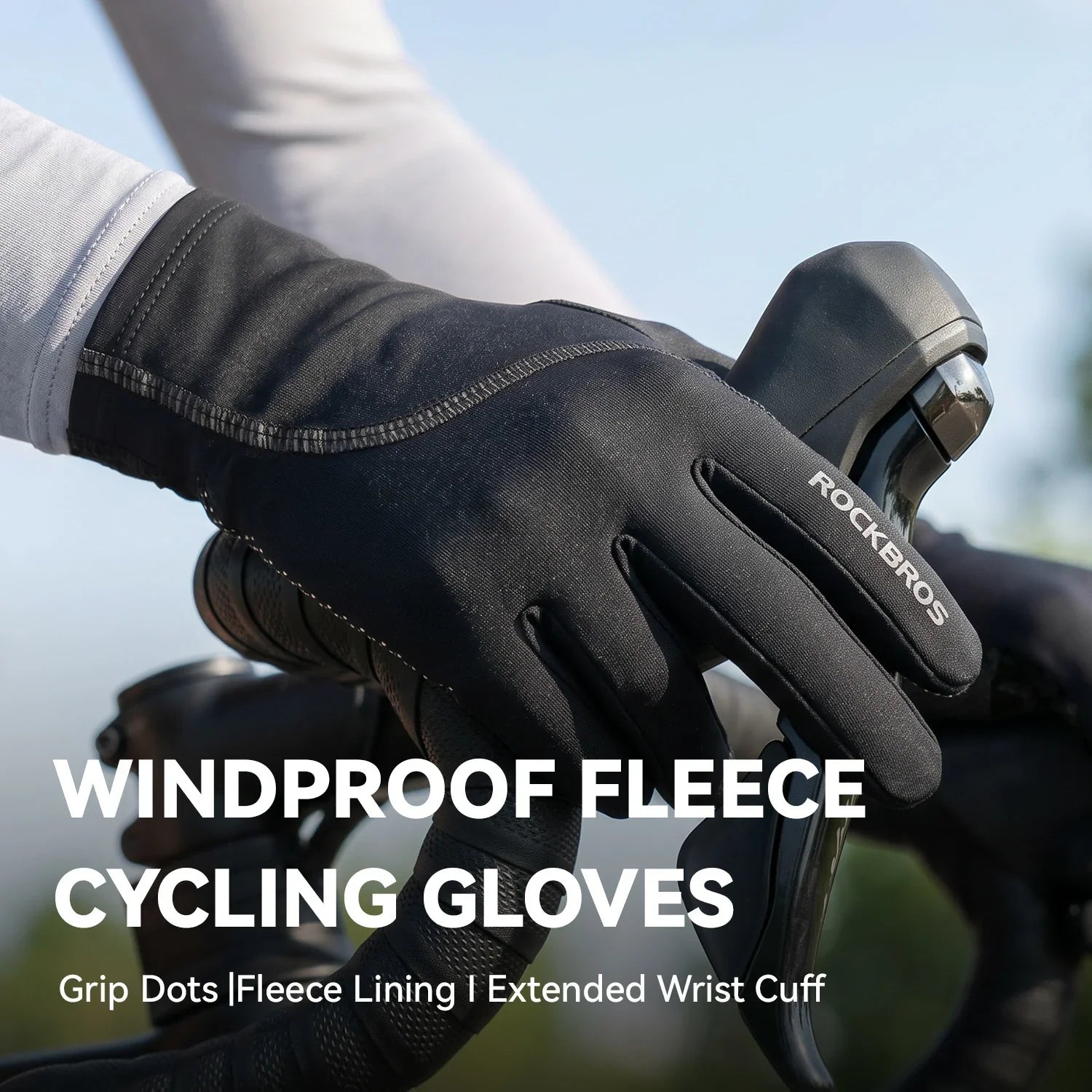 A close-up of a person's hand wearing a black RockBros windproof fleece cycling glove while gripping a bicycle handlebar, with outdoor sky and blurred scenery in the background and text overlay reading 'WINDPROOF FLEECE CYCLING GLOVES'.