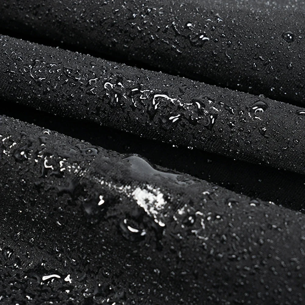 Close-up of a black waterproof fabric surface with water droplets beaded on top, showing the material texture and water-repellent finish.