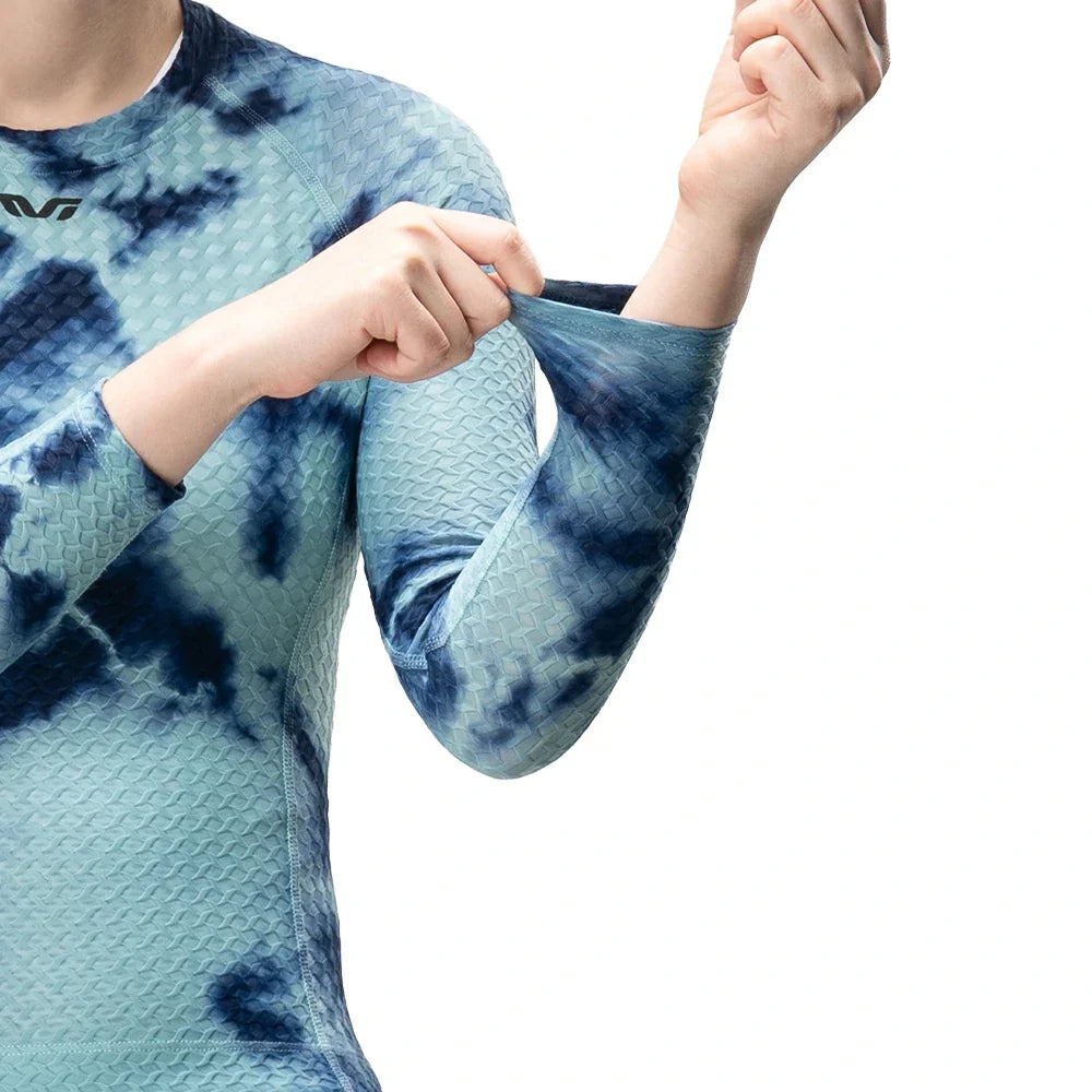A close-up of a person wearing a long-sleeve textured athletic top with a blue and teal tie-dye pattern, stretching the fabric at the cuff against a white background.